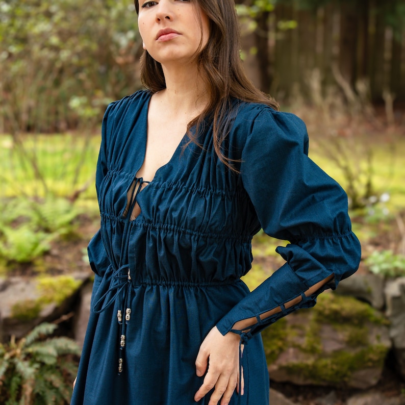 May include: A dark blue, long-sleeved dress with a gathered bodice and a lace-up detail at the neckline. The dress has a fitted waist and a flowing skirt.