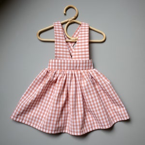 Könnte beinhalten: Ein rosa-weißes Gingham-Kleid mit einem Kreuzrücken und einem gerafften Rock.