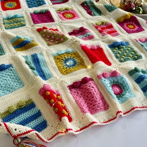 May include: A white crocheted blanket with a red border and a colorful tassel. The blanket is made up of squares with different patterns, including stripes, polka dots, and flowers. The blanket is perfect for a cozy winter night.
