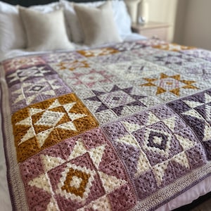 Peut inclure: Une couverture en crochet avec un motif patchwork compos&eacute; de diff&eacute;rentes formes g&eacute;om&eacute;triques dans des tons de violet, rose, blanc et or.