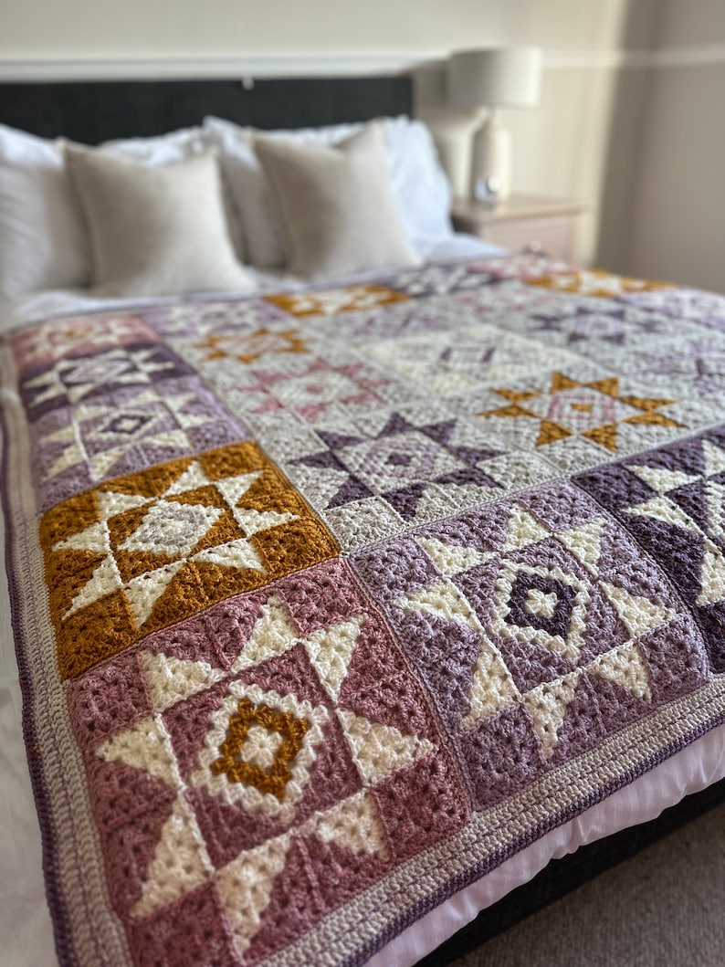 Peut inclure: Une couverture en crochet avec un motif patchwork compos&eacute; de diff&eacute;rentes formes g&eacute;om&eacute;triques dans des tons de violet, rose, blanc et or.