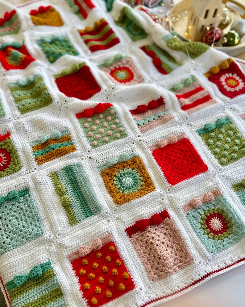 May include: A white crochet blanket with a variety of colorful squares featuring different Christmas gift designs. The squares are made with different stitches and textures, including polka dots, stripes, and flowers.