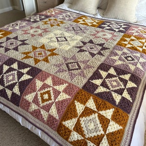 Peut inclure: Une couverture en crochet avec un motif g&eacute;om&eacute;trique dans les tons de violet, rose, blanc et marron. La couverture est compos&eacute;e de carr&eacute;s avec diff&eacute;rents motifs d'&eacute;toiles et de diamants.