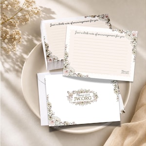 Peut inclure: Ensemble de papeterie avec des bordures florales et le texte "Juste un petit mot d'encouragement pour vous" et "Please visit JW.ORG". L'ensemble comprend des blocs-notes et des enveloppes, disposés sur une assiette blanche.