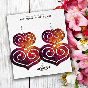 May include: A pair of double heart shaped earrings with a swirling pattern in shades of pink, orange, and yellow. The earrings are made of a textured material that resembles metal.