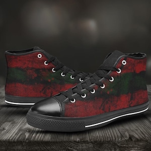 以下が含まれることがあります： 赤、黒、緑の飛び散ったペイントデザインが施された、黒色のハイカットキャンバススニーカーのペアです。