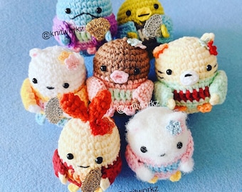 May include: Seven crocheted amigurumi plushies in various colours and designs, including a blue bird, a yellow bird, a brown bear, a white cat, a yellow bunny, a white cat, and a tiger. The plushies are holding small golden fans. The plushies are on a light blue background. The text "@knitworkz" is visible in the image.
