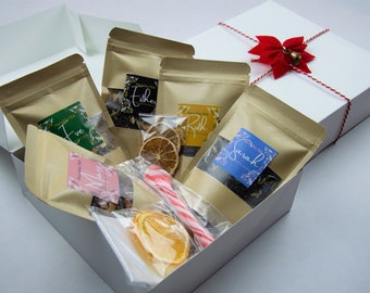 May include: A white gift box with a red ribbon and bow, containing five brown paper bags with tea labels that say "Eve", "Ethel", "Ruth", "Sarah", and "Mary". The box also contains dried orange slices, a candy cane, and a small white bag.