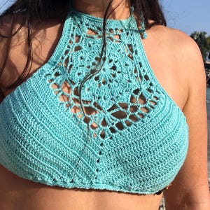 May include: A turquoise crochet halter top with a delicate lace pattern. The top is made with a fine yarn and has a loose, flowy fit.