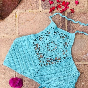 Könnte beinhalten: Ein hellblaues Häkel-Halter-Top mit einem großen, filigranen Blumendesign in der Mitte. Das Top ist aus einem zarten, offenen Stichmuster gefertigt.