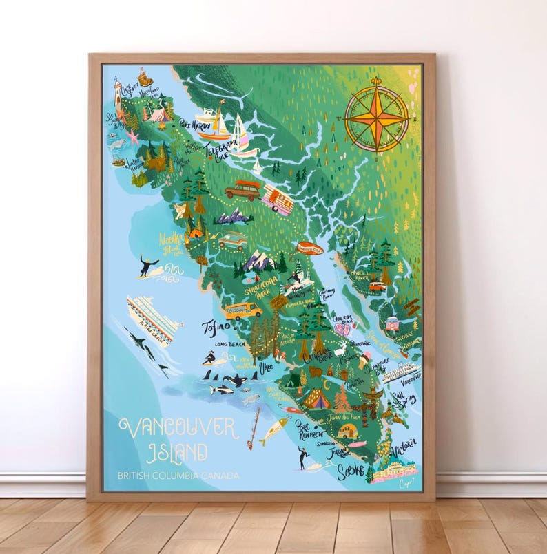 May include: A framed map of Vancouver Island, British Columbia, Canada, with a light brown wooden frame. The map is illustrated with green, blue, and yellow colors, featuring landmarks, icons, and the text "Vancouver Island". A compass rose is in the upper right corner.