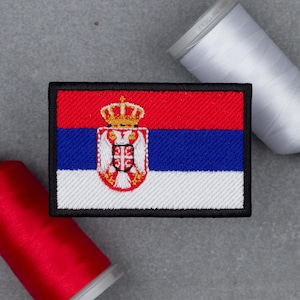 Puede incluir: Un parche rectangular bordado con la bandera de Serbia de franjas horizontales roja, azul y blanca. Una corona dorada detallada se sitúa sobre un emblema de águila bicéfala blanca con un escudo rojo, una cruz blanca y cuatro eslabones.