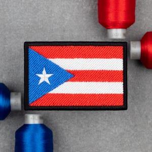 Può includere: Toppa ricamata raffigurante la bandiera di Porto Rico. La toppa rettangolare ha un triangolo blu con una stella bianca e strisce rosse e bianche alternate. La toppa è circondata da un bordo nero. Sullo sfondo ci sono rocchetti di filo rosso e blu.