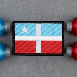 Peut inclure: Écusson brodé avec un motif de drapeau. La partie supérieure est bleu clair, la partie inférieure rouge, avec une croix blanche. Une étoile blanche est dans le coin supérieur gauche. Le patch a une bordure noire.