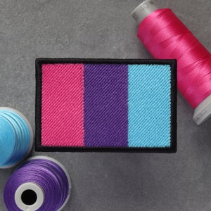 Könnte beinhalten: Ein gestickter Patch in Pink, Lila und Blau mit schwarzem Rand. Der Patch ist eine Darstellung der Genderqueer-Pride-Flagge.