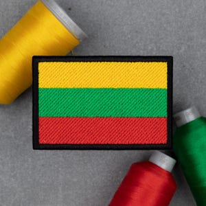 May include: Embroidered patch featuring the flag of Lithuania, with horizontal stripes of yellow, green, and red, outlined in black. The patch is rectangular and surrounded by spools of yellow, red, and green thread.