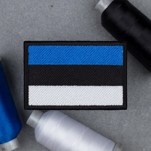 Puede incluir: Parche bordado con la bandera de Estonia. El parche rectangular muestra franjas horizontales azules, negras y blancas, con un borde negro. Carretes de hilo azul, negro y blanco rodean el parche.