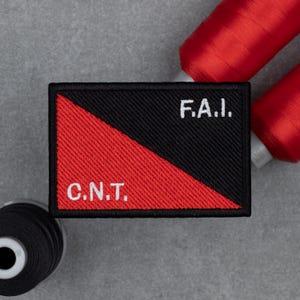 Peut inclure: Écusson rectangulaire brodé avec un motif diagonal noir et rouge. Le patch porte le texte blanc "C.N.T." sur la section rouge et "F.A.I." sur la section noire. Des bobines de fil rouge sont visibles en arrière-plan.