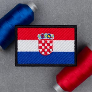 May include: A rectangular embroidered patch featuring the Croatian flag with horizontal red, white, and blue stripes and a central coat of arms with a red and white checkered shield topped by a five-part crown, bordered by a thick black edge.