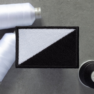 Pode incluir: Um remendo bordado em preto e branco com uma linha diagonal que divide o remendo. O remendo é rodeado por fio branco.