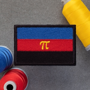 Könnte beinhalten: Ein gestickter Patch in Blau, Rot und Schwarz mit einem gelben "π"-Symbol in der Mitte.