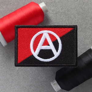 Può includere: Toppa ricamata nera e rossa con un simbolo di anarchia bianco, "A" all'interno di un cerchio.