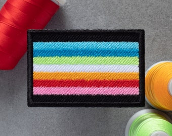 May include: A black embroidered patch with a multi-colored striped design. The stripes are blue, green, white, orange, red, and pink.