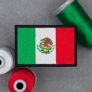 Peut inclure: Écusson brodé représentant le drapeau mexicain, avec des rayures verticales vertes, blanches et rouges et les armoiries mexicaines. L'écusson est bordé de noir. Des bobines de fil vert, blanc et rouge sont en arrière-plan.