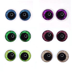Peut inclure: Une collection de six paires d'yeux artisanaux scintillants de diff&eacute;rentes couleurs. Les yeux ont une pupille noire avec un contour blanc et sont entour&eacute;s de paillettes bleues, violettes, vertes, rouges, jaune-vert et dor&eacute;es.