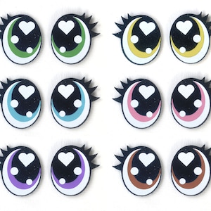 May include: Set of twelve colorful plastic eyes with black pupils and white hearts. Each eye has a different colored rim, including green, yellow, blue, pink, purple, and brown.