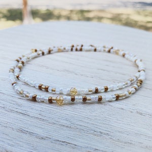 May include: A double strand beaded necklace with white and gold beads. The necklace is made with small, round beads and has a delicate, minimalist style.
