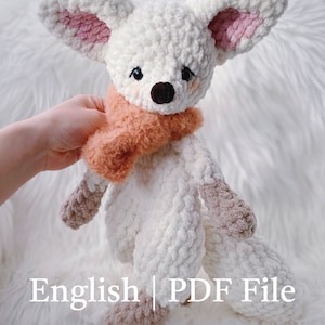 May include: White crocheted fox plush toy with pink ears and a brown and orange scarf. The toy is sitting on a white fluffy surface. English PDF File.