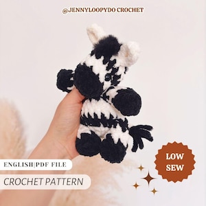 May include: A small, plush, black and white crocheted zebra toy with a fuzzy texture. The image includes text that reads @JENNYLOOPYDO CROCHET, ENGLISH|PDF FILE, CROCHET PATTERN, and LOW SEW with decorative star icons.