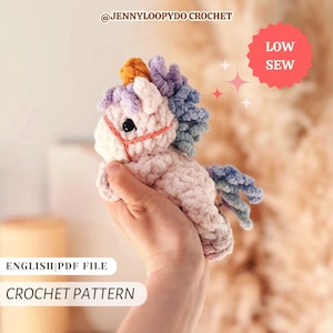 May include: A small, plush, light pink crochet unicorn toy with a golden horn, a multi-coloured mane and tail in shades of purple and blue, and black safety eyes. The text reads @JENNYLOOPYDO CROCHET, LOW SEW, ENGLISH|PDF FILE, and CROCHET PATTERN.