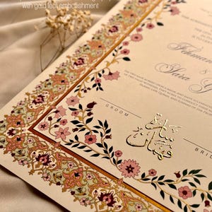 Pu&ograve; includere: Un invito di nozze con intricati disegni floreali in oro, rosa e verde. I nomi della coppia sono scritti in calligrafia araba in foglia d'oro. Il testo recita "Couple's names in Arabic Calligraphy with gold leaf embellishment".