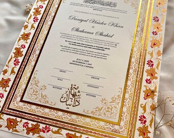 Może przedstawiać: Ozdobny akt ślubu ze złotymi i czerwonymi kwiatowymi akcentami. Dokument zawiera ozdobne obramowania i tekst w języku angielskim i arabskim. Akt ślubu jest dla Daniyal Haider Khan i Shahama Shahid.