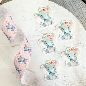 Könnte beinhalten: Eine Rolle rosa-weiß gestreiftes Band mit einem sich wiederholenden Muster aus grauen Elefanten und floralen Akzenten. Mehrere elefantenförmige Aufkleber mit Blumenkränzen sind auf einer weißen Oberfläche verstreut.