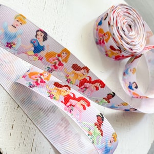 Puede incluir: Cinta blanca con ilustraciones coloridas de princesas de Disney. La cinta se muestra enrollada y desenrollada, mostrando a los personajes en varias poses. Ideal para manualidades, envolver regalos o a&ntilde;adir un toque m&aacute;gico a cualquier proyecto.