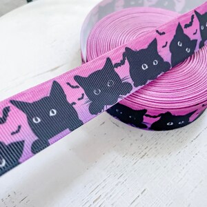 K&ouml;nnte beinhalten: Eine Rolle lila Band mit einem sich wiederholenden Muster aus schwarzen Katzen-Silhouetten und Flederm&auml;usen. Das Band hat einen Farbverlauf, der von Schwarz zu Lila &uuml;bergeht. Dieses dekorative Band ist ideal f&uuml;r Halloween-Bastelarbeiten und Geschenkverpackungen.