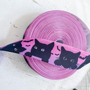 K&ouml;nnte beinhalten: Eine Rolle rosa Band mit einem Muster aus schwarzen Katzen und Flederm&auml;usen. Das abgerollte Band zeigt schwarze Katzensilhouetten und Flederm&auml;use vor einem rosa-violetten Farbverlauf. Geeignet f&uuml;r Bastelarbeiten oder zum Geschenkeverpacken.