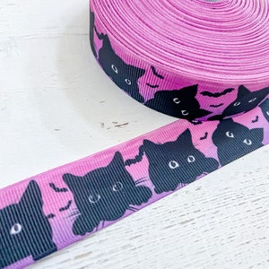 K&ouml;nnte beinhalten: Eine Rolle rosa Band mit einem sich wiederholenden Muster aus schwarzen Katzen-Gesichtern und Flederm&auml;usen. Das Band hat einen leuchtenden Rosaton, der zu einem helleren Farbton verblasst und einen Farbverlauf erzeugt. Das Design mit schwarzen Katzen und Flederm&auml;usen ist ideal f&uuml;r Halloween-Bastelarbeiten.