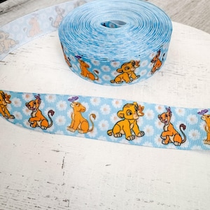 May include: A roll of light blue ribbon featuring a repeating pattern of cartoon lion cubs and white daisies. The ribbon is made of a soft, textured material and is suitable for crafts, gift wrapping, or party decorations.