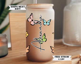 May include: A frosted glass tumbler with a bamboo lid and straw. The tumbler has a personalized name "Alexandra" written in black cursive script and is decorated with colorful butterfly stickers.