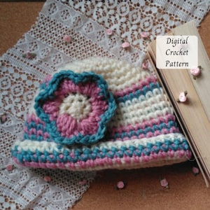 May include: A crocheted hat with a large flower applique. The hat features stripes of white, pink, and teal. The flower is pink with a teal outline. The text "Digital Crochet Pattern" is visible on a wooden surface.