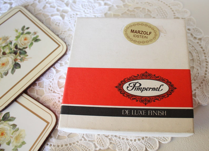 May include: A white box with a red and black stripe. The box has the text "Pimpernel De Luxe Finish" and a sticker that says "Marzolf Idstein".