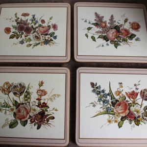 K&ouml;nnte beinhalten: Set aus vier quadratischen Tischsets mit Blumendesigns. Jedes Tischset hat einen cremefarbenen Hintergrund mit einer anderen Anordnung von Rosen, Tulpen und anderen Blumen in Rosa-, Rot- und Lilat&ouml;nen. Die R&auml;nder sind mit einem hellbraunen Rand versehen.