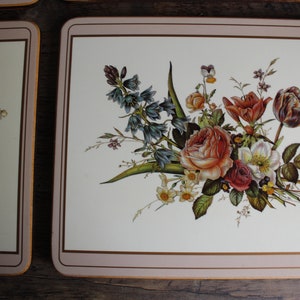K&ouml;nnte beinhalten: Rechteckige Tischsets mit floralen Designs. Die Tischsets haben einen cremefarbenen Hintergrund mit einem Rand und zeigen einen Strau&szlig; aus Rosen, Tulpen und anderen Blumen in Rot-, Orange- und Wei&szlig;t&ouml;nen.