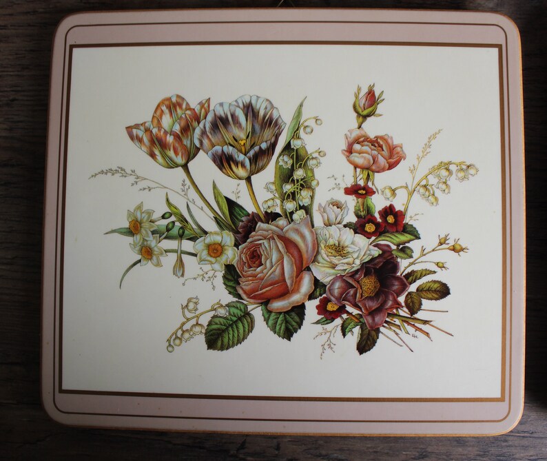 K&ouml;nnte beinhalten: Ein quadratischer Platzdeckchen mit floralem Design. Das Bild zeigt einen Strau&szlig; aus Rosen, Tulpen und anderen Blumen in Rosa-, Wei&szlig;- und Burgundert&ouml;nen. Der Platzdeckchen hat einen cremefarbenen Hintergrund mit einem rosa Rand.