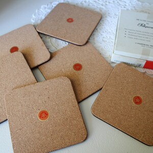 May include: Set of six cork coasters with a red and gold logo that says "Rippner" in a white circle. The coasters are in a white box with red and black trim. The box says "Deluxe Coasters by Rippner".