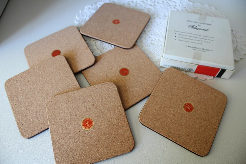 May include: Set of six cork coasters with a red and gold logo that says "Rippner" in a white circle. The coasters are in a white box with red and black trim. The box says "Deluxe Coasters by Rippner".